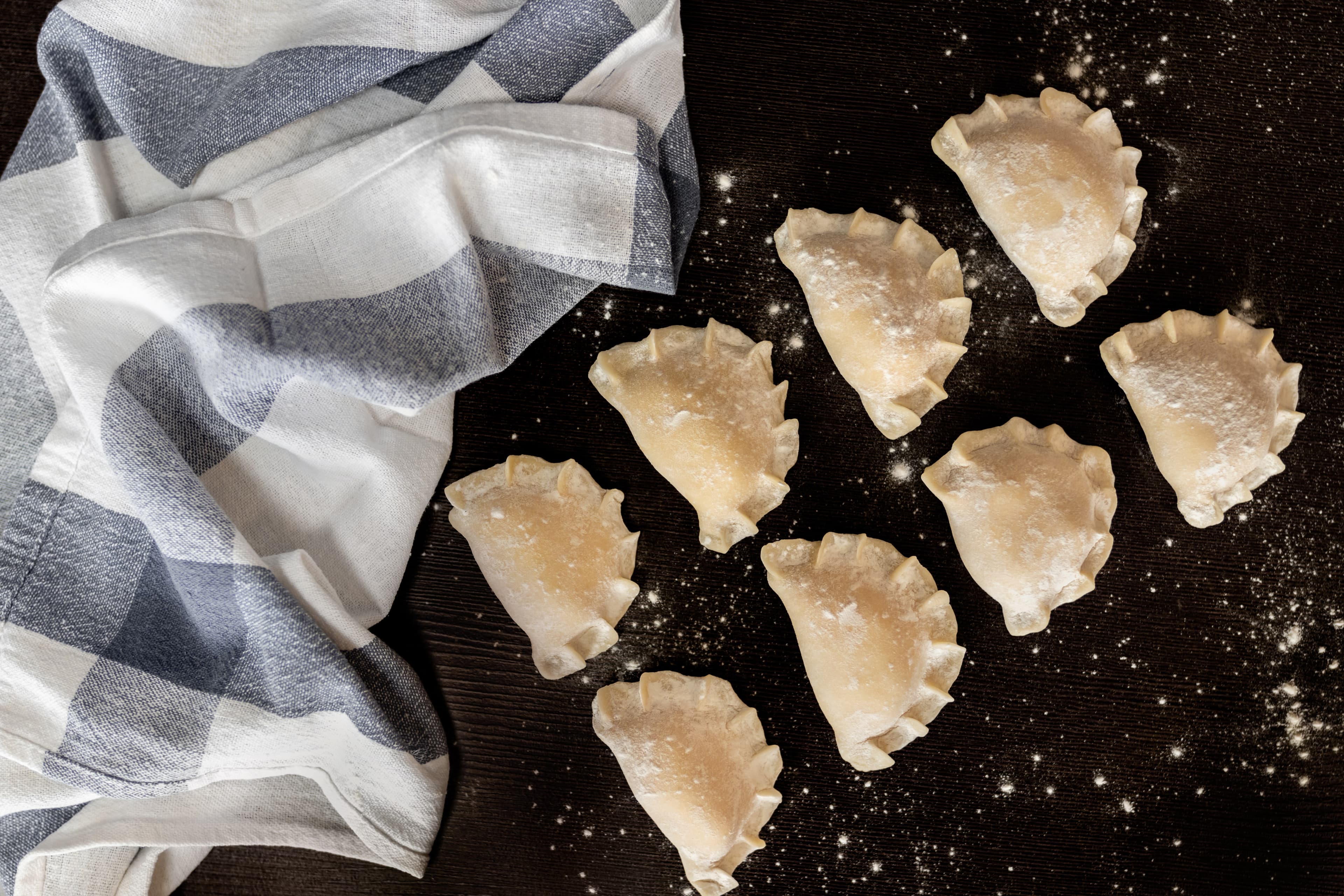 Świeżo ulepione pierogi na omączonym ciemnym blacie